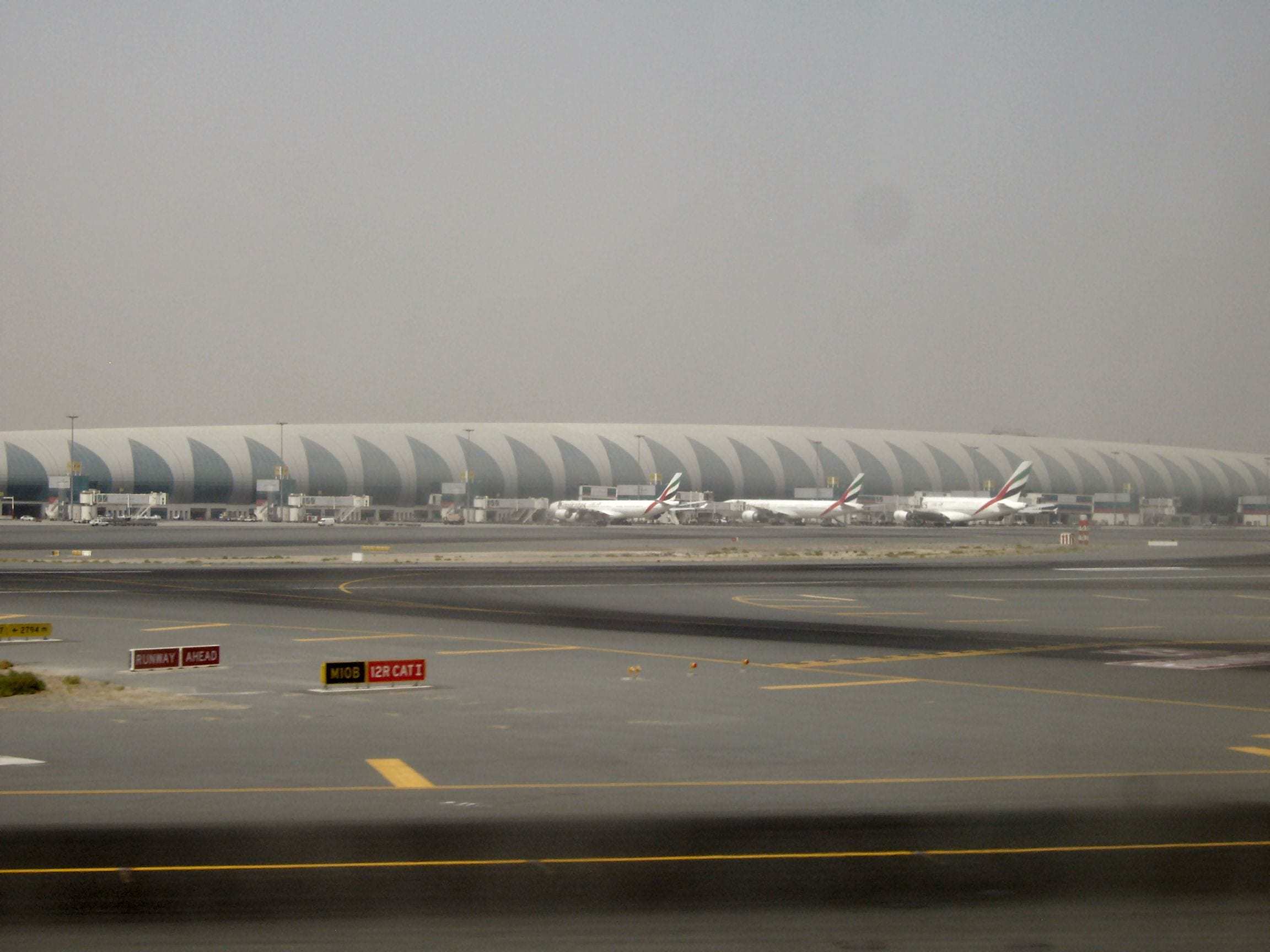 The long ribbed roof of Dubai International Airport Terminal 3 lined with Emirates jets on a hazy day in Dubai