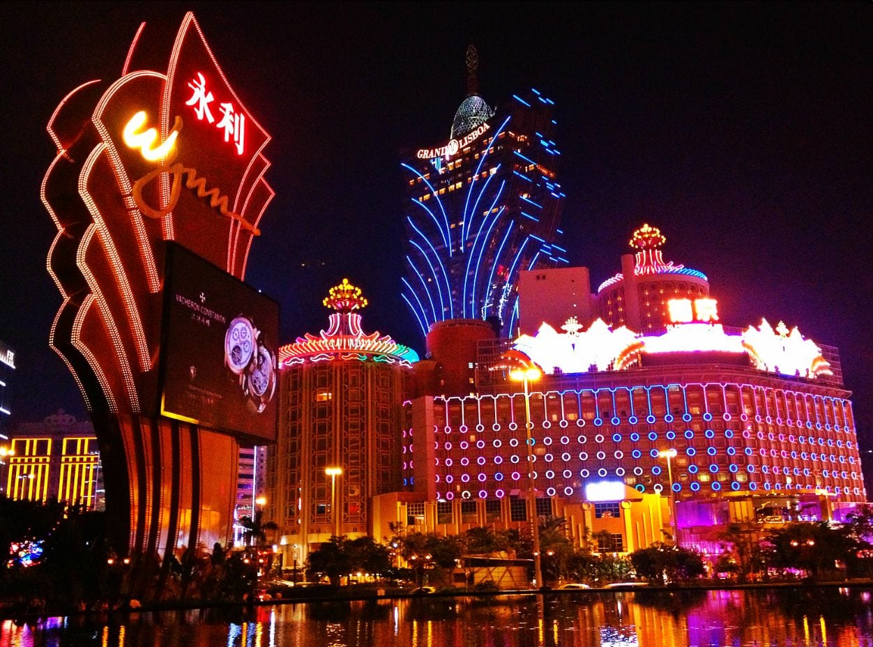 Neon casino signs and illuminated hotel towers reflected in dark water on the Macau waterfront at night