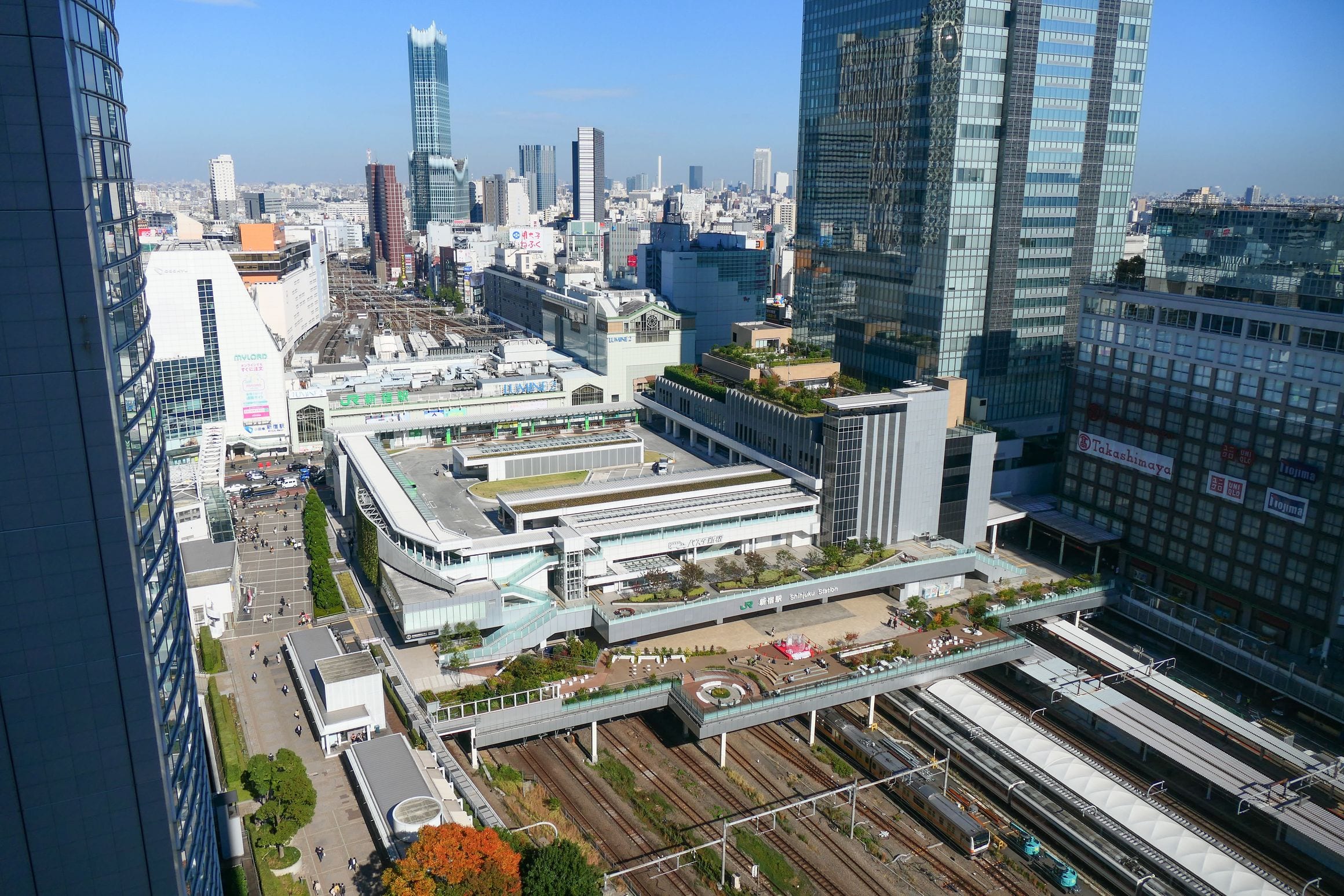 Elevated view of Shinjuku Station in Tokyo, its rail tracks running beneath the New South Exit and Lumine buildings amid skyscrapers