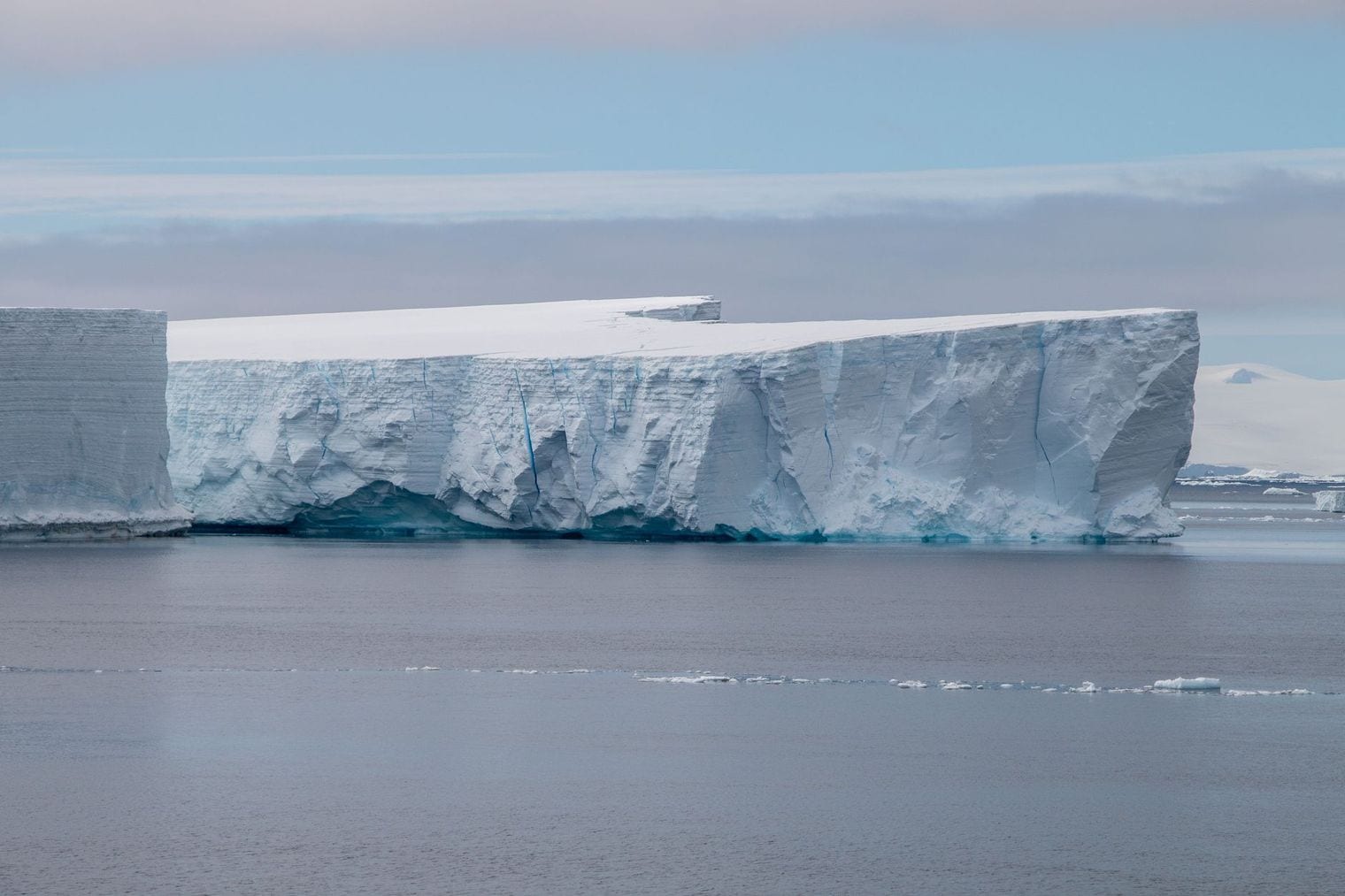 Sheer ice cliffs of a tabular iceberg rising from still Antarctic water beneath a pale sky