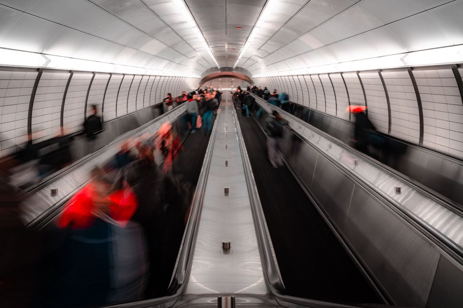 Escalators descending into an arched metro tunnel, with commuters blurred into streaks by a long exposure