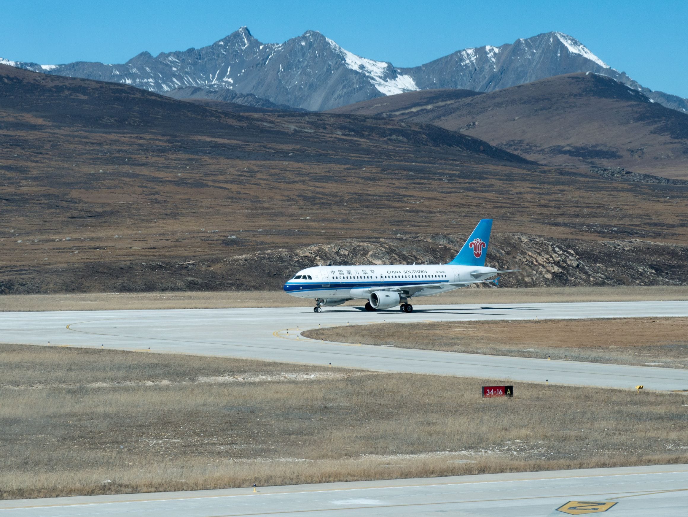 A China Southern jet taxiing at Daocheng Yading Airport on the barren Tibetan Plateau, with snowcapped peaks of Sichuan rising behind