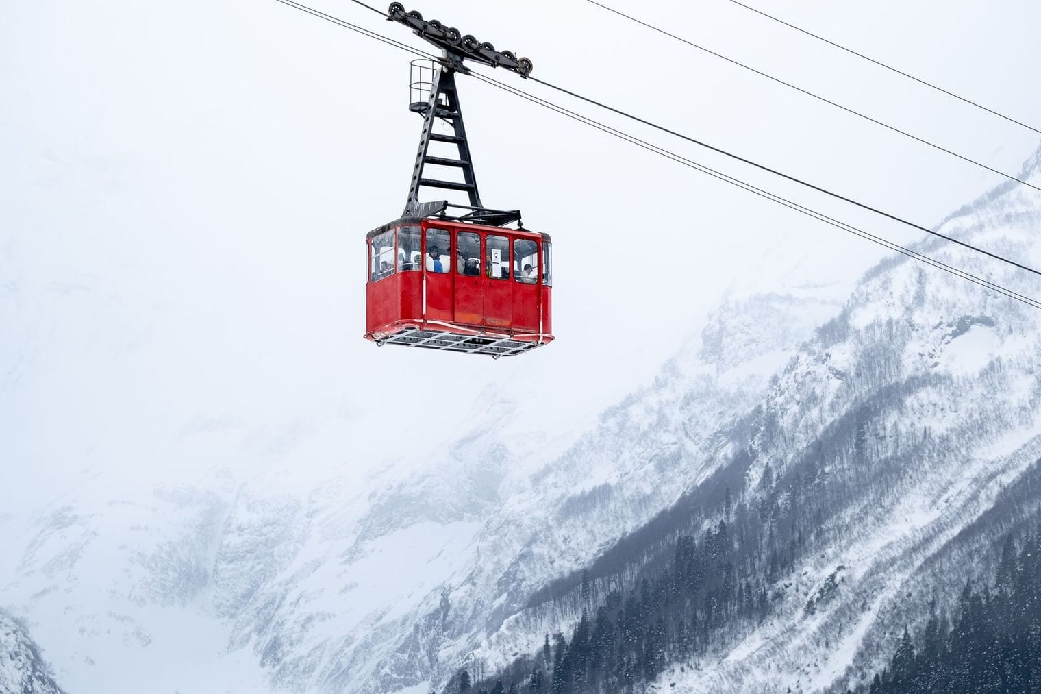 A red aerial tramway cabin hanging from its cable in front of a mist-shrouded snow-covered mountainside
