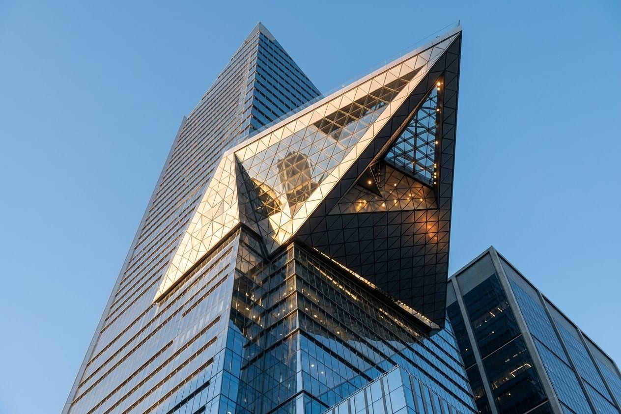 Visitor looking out through the floor-to-ceiling glass of a high observation deck at sunset