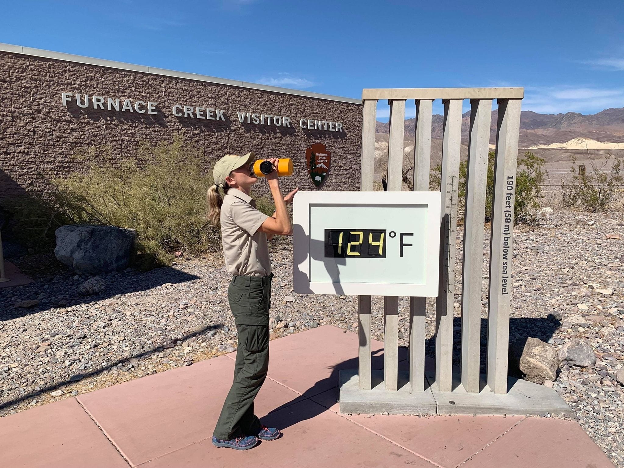 A park ranger drinks water beside the famous thermometer reading 124°F outside the Furnace Creek Visitor Center in Death Valley, California