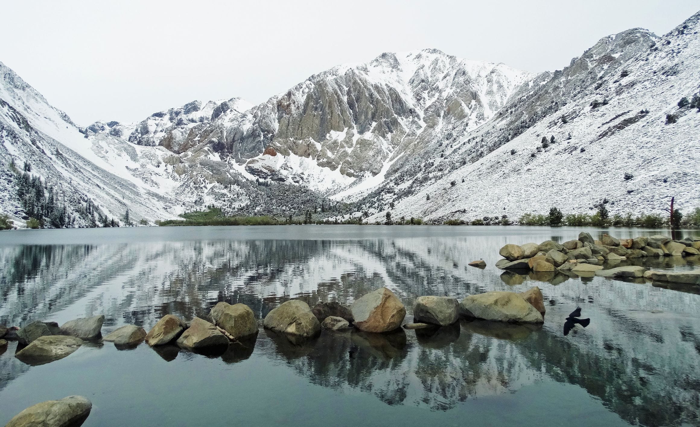 Snow-covered Sierra Nevada peaks reflected in the still water of an alpine lake in eastern California