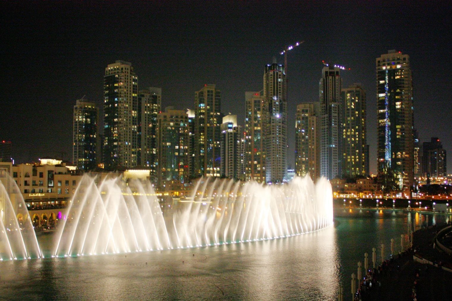 The Dubai Fountain lit up at night in front of the Downtown Dubai towers.