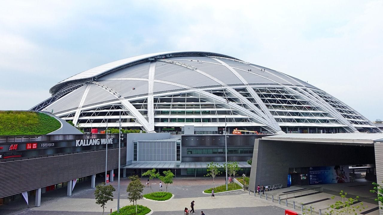 The domed roof of the Singapore National Stadium rising above the still water of the Kallang Basin, seen past a low road bridge in monochrome