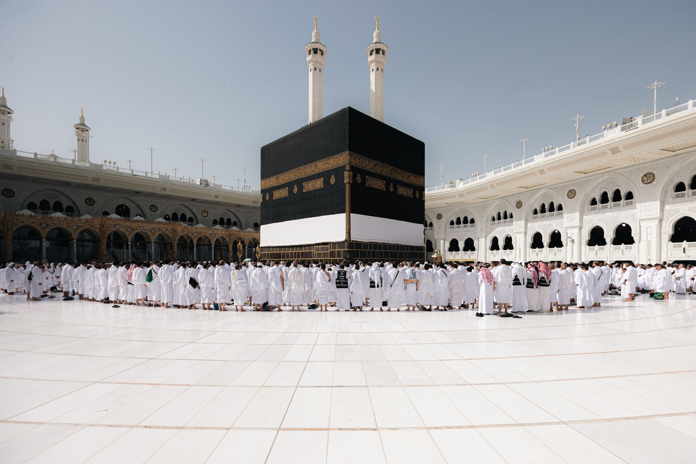 Worshippers in white lining the marble courtyard around the Kaaba beneath the arcades and minarets of Masjid al-Haram in Mecca