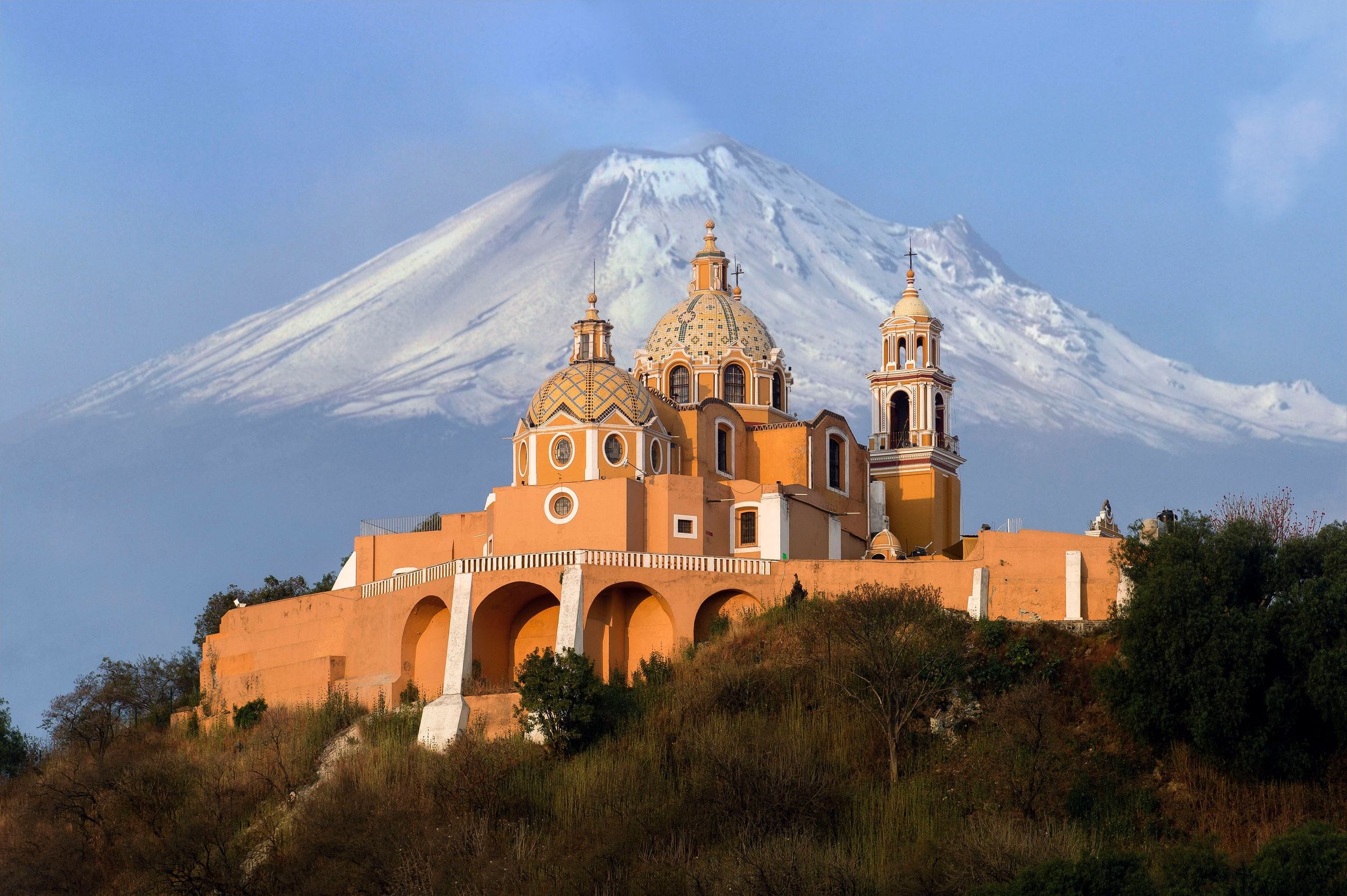 The Church of Our Lady of Remedies atop the grassy mound of the Great Pyramid of Cholula, with snowy Popocatépetl behind, in Puebla