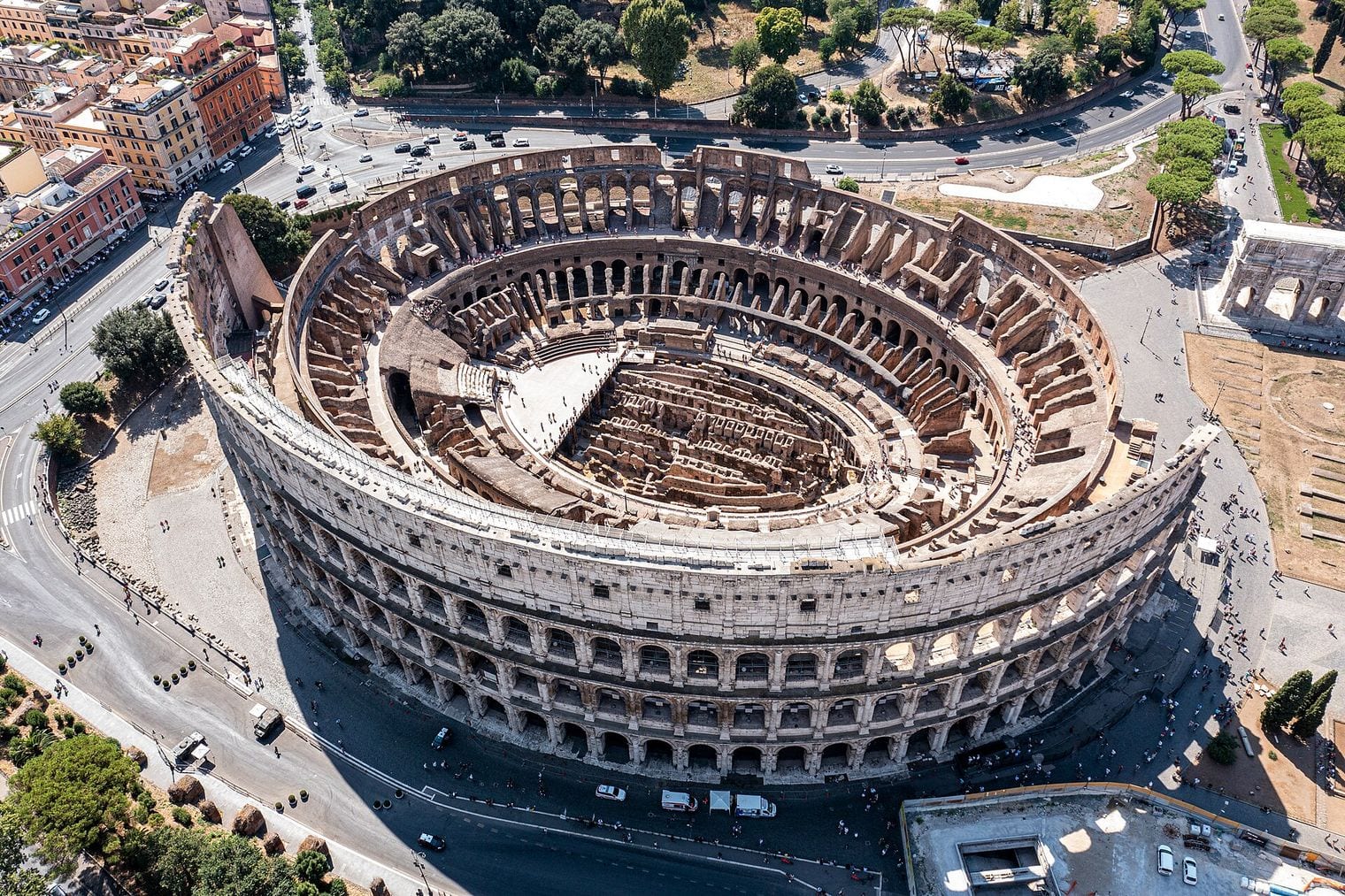 Aerial view of the Colosseum in Rome, its full ellipse of arcaded tiers open to the excavated hypogeum on the arena floor below.