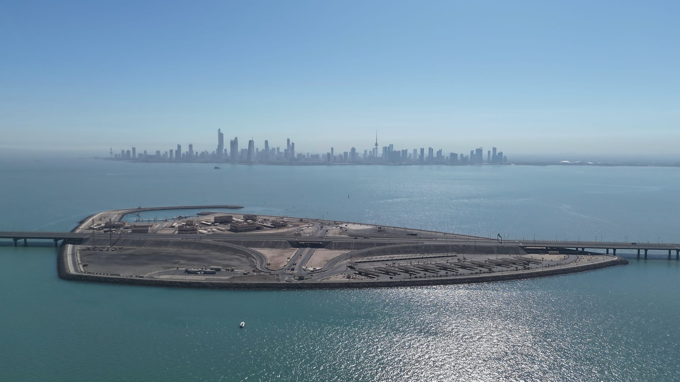 Aerial view of the Sheikh Jaber Al-Ahmad Al-Sabah Causeway crossing its artificial island in Kuwait Bay, with the Kuwait City skyline beyond