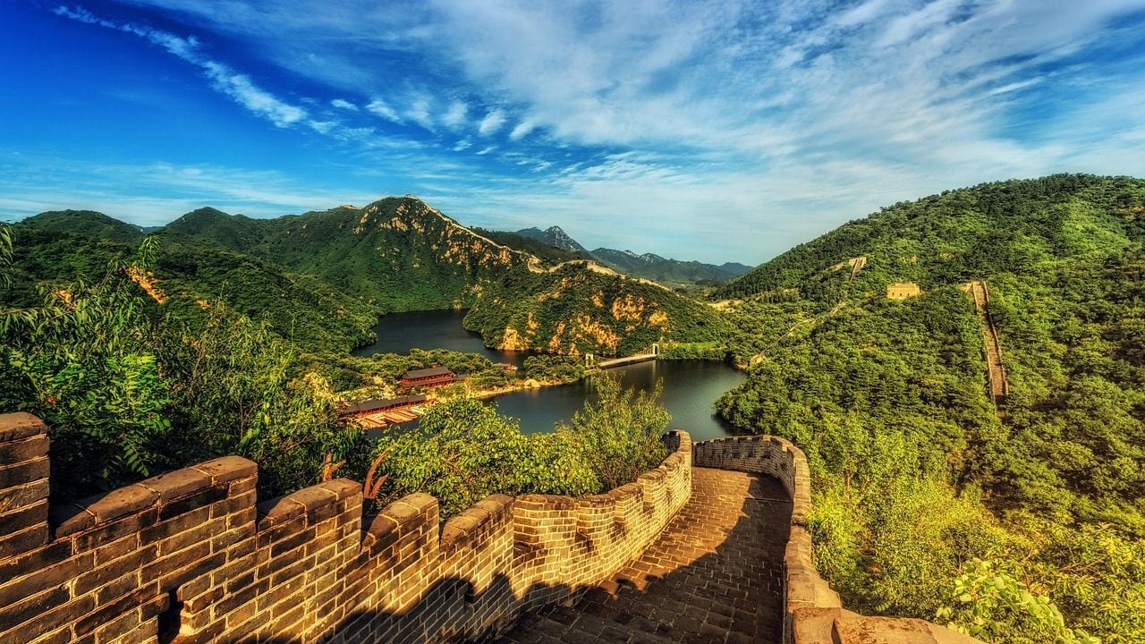 Brick battlements of the Great Wall of China curving along a forested mountain ridge above a reservoir.