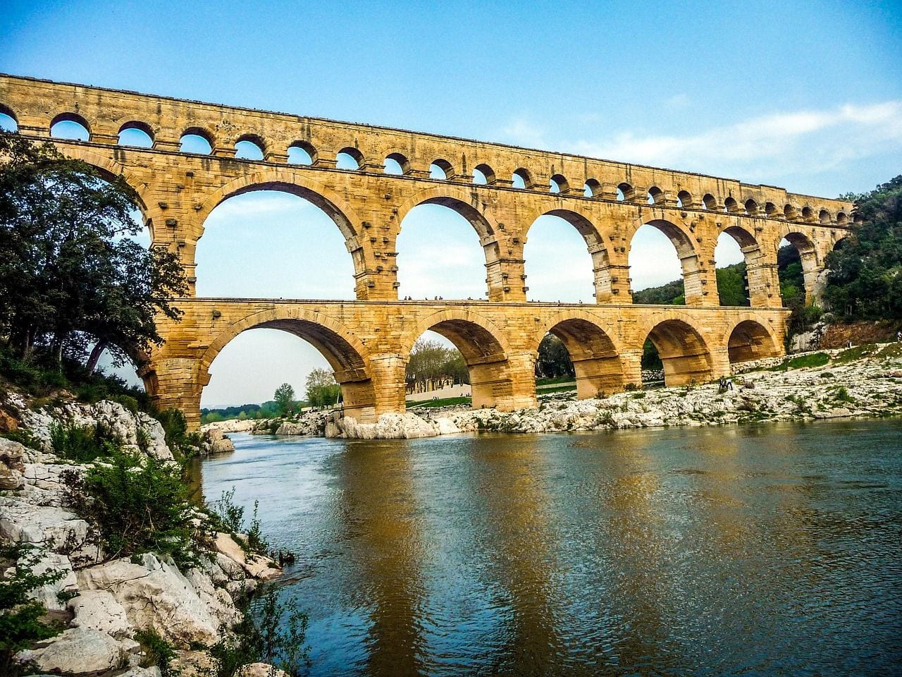 The three tiers of golden limestone arches of the Pont du Gard Roman aqueduct bridge spanning the Gardon river valley in southern France