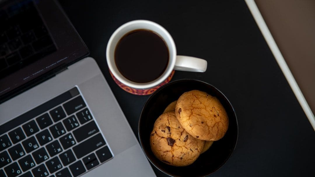 A bowl of cookies and a cup of coffee beside a laptop