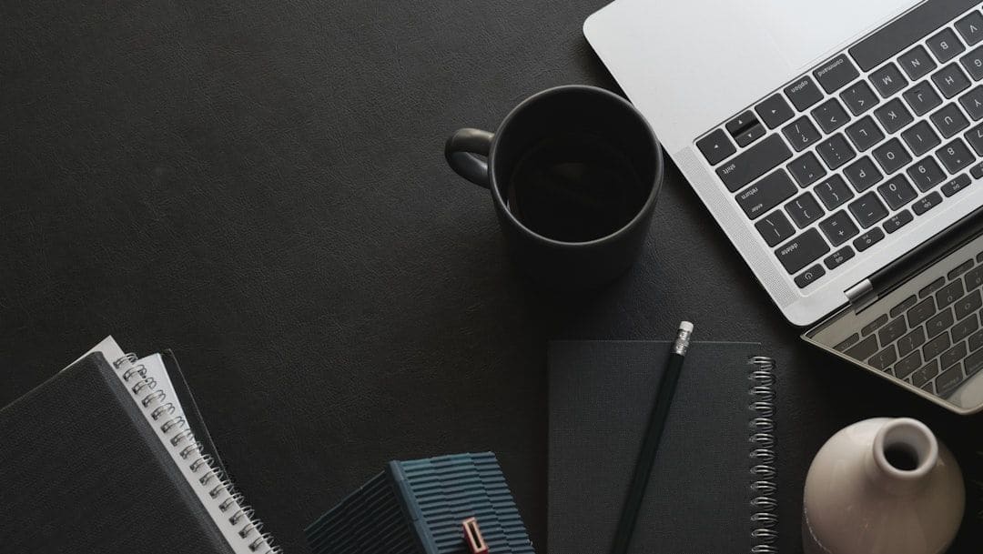 Writing on a laptop at a desk with a notebook and coffee