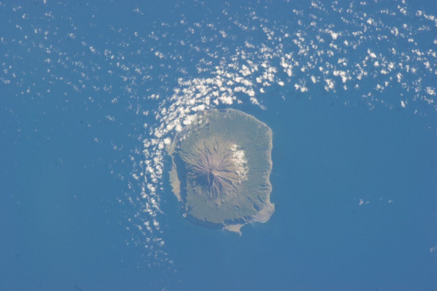 The volcanic cone of Tristan da Cunha photographed from orbit, a single circular island ringed by cloud and surrounded by open ocean in the South Atlantic.