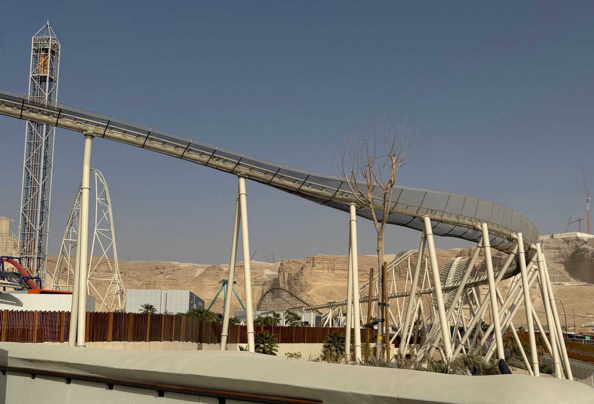 The mesh-covered track of Falcon's Flight arcing into its final turn against the desert escarpment at Six Flags Qiddiya City, Saudi Arabia