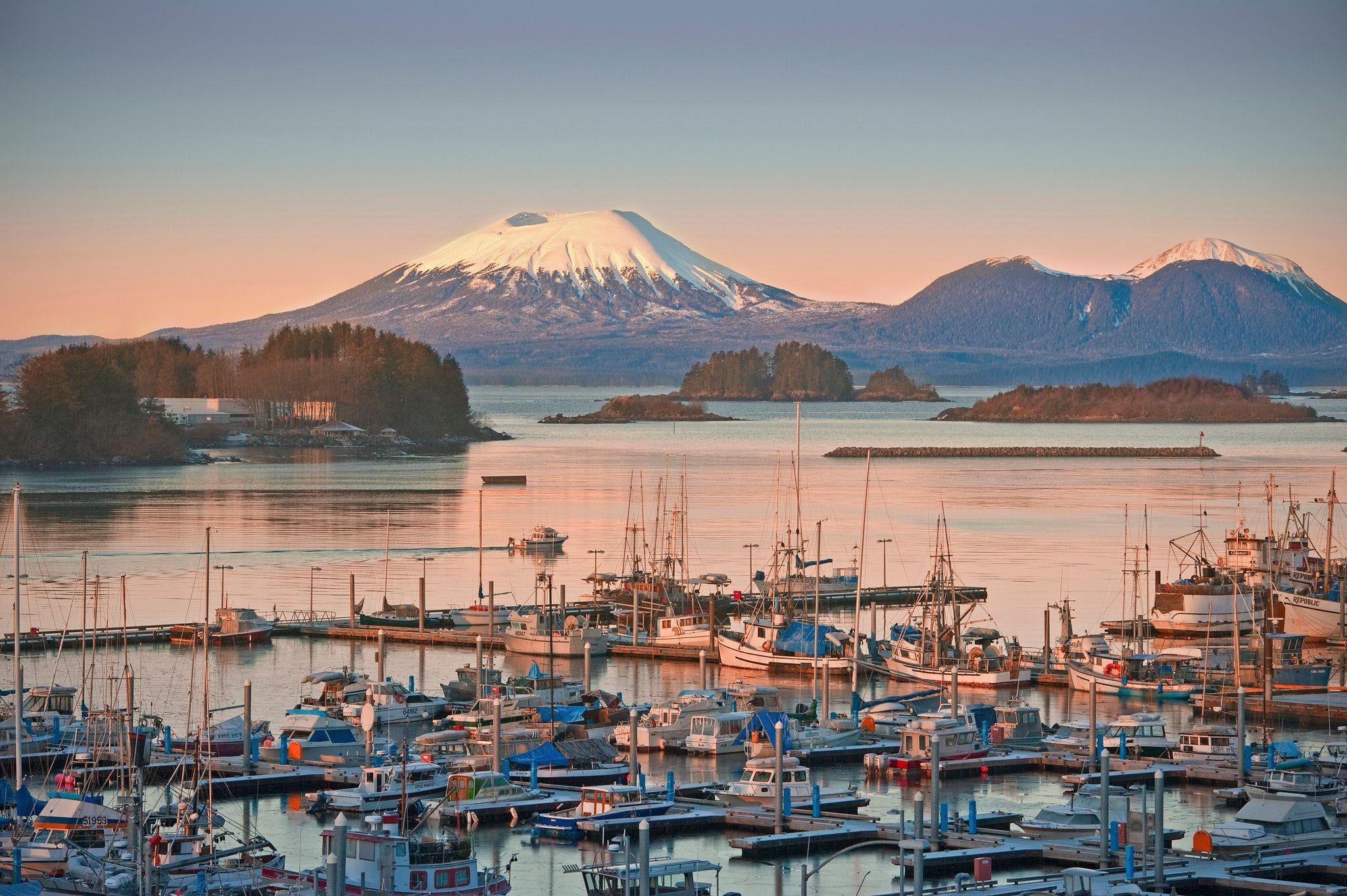 Fishing boats in Sitka harbor at sunset beneath the snow-capped cone of Mount Edgecumbe, Alaska