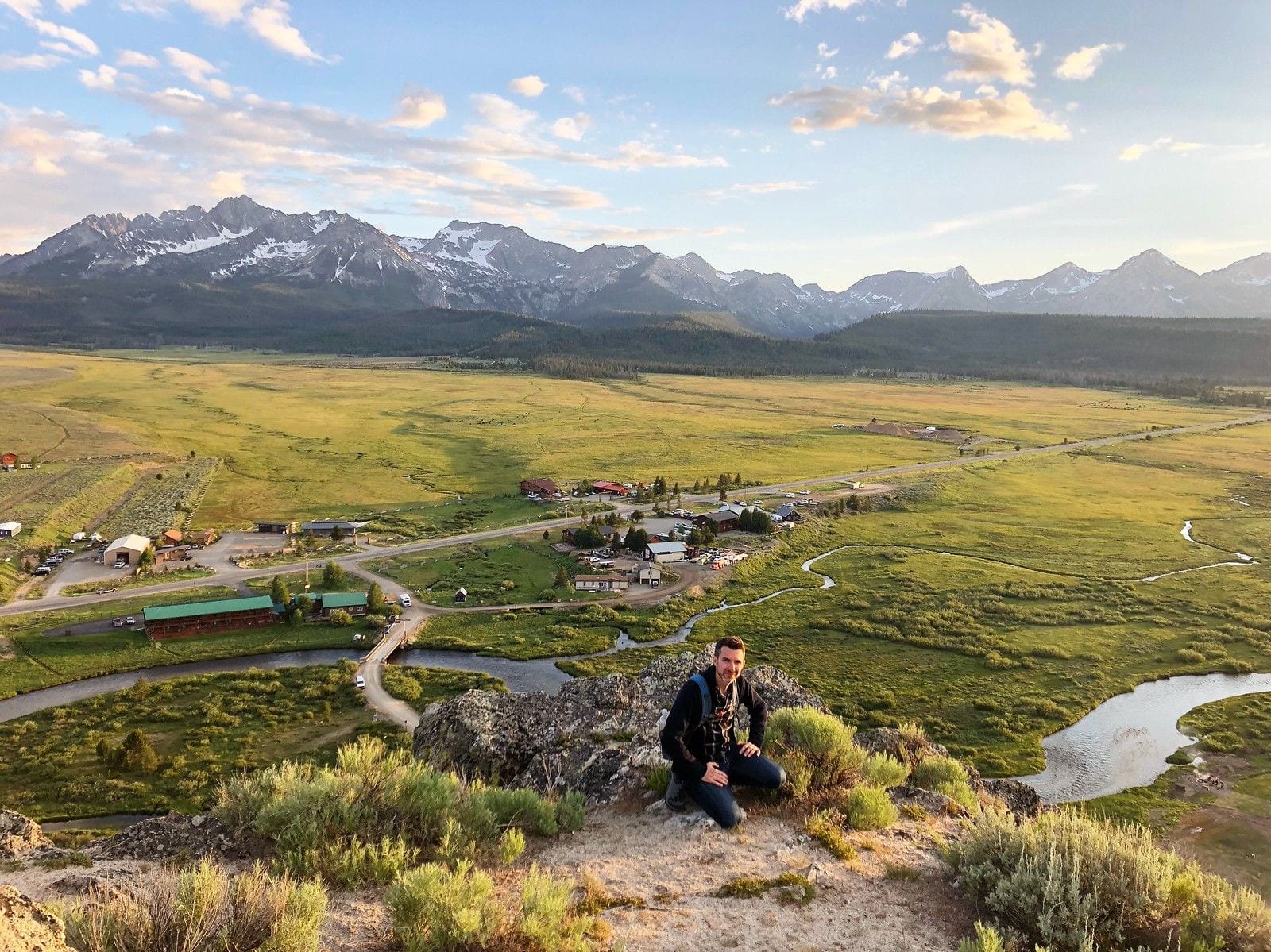 The tiny mountain town of Stanley, Idaho, in the Sawtooth Valley at sunset, with the jagged Sawtooth Mountains rising behind it and a river winding across the meadow
