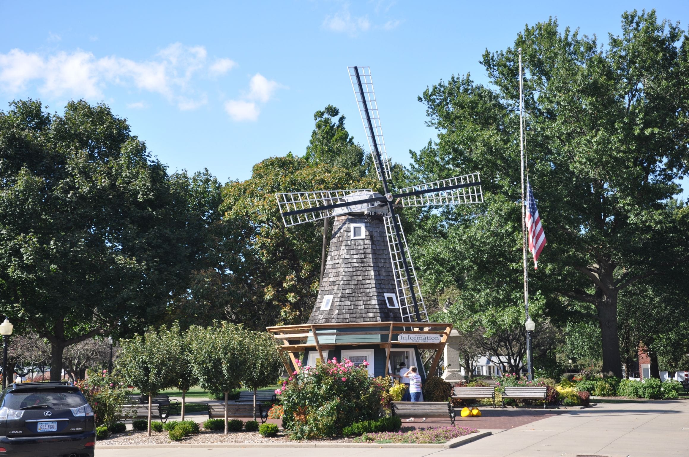 Dutch-style windmill and flower beds at the Pella Information Center in Pella, Iowa, framed by shade trees under a blue sky