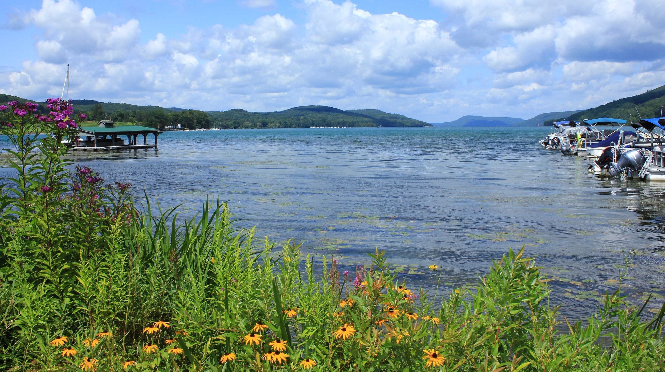 Otsego Lake at Cooperstown, New York, with docks and boats and wooded hills across the water