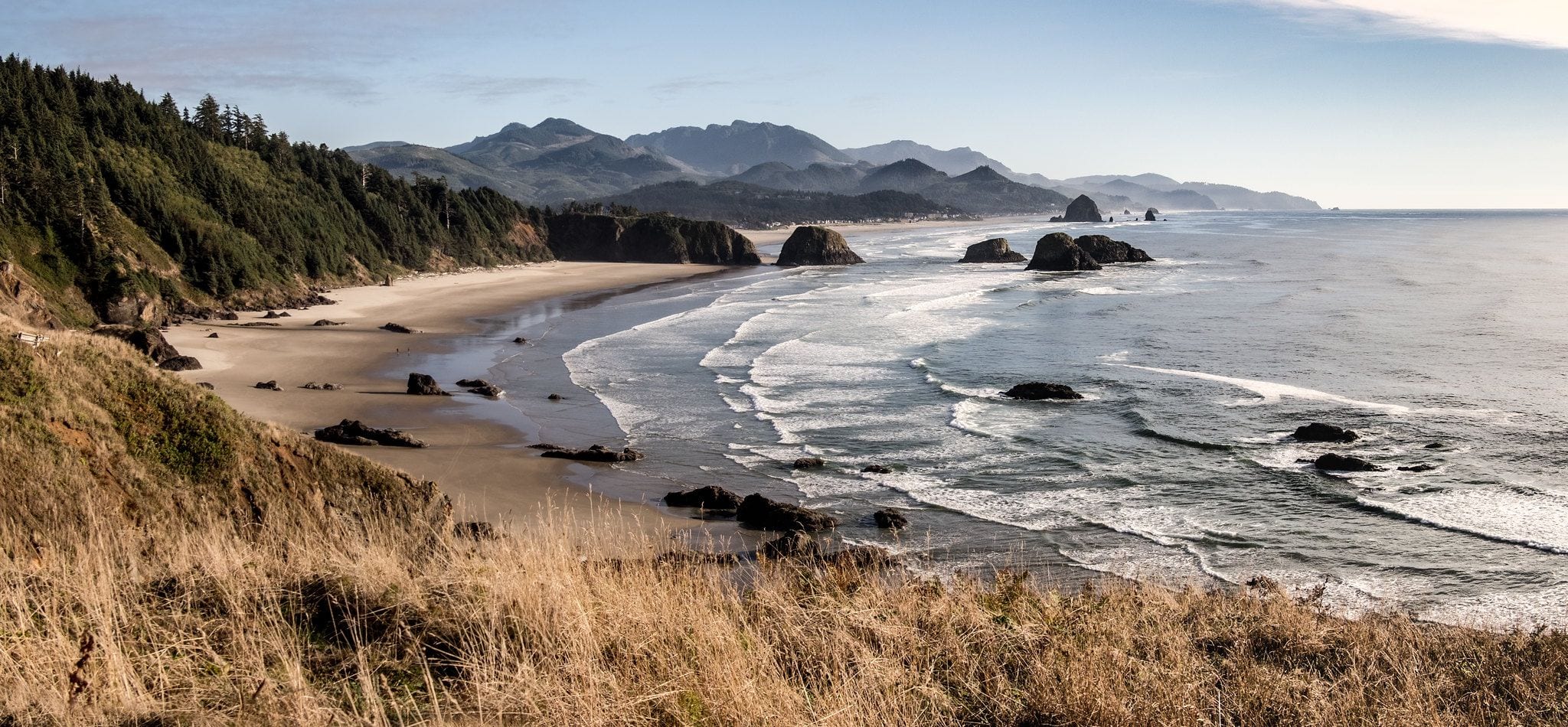 Haystack Rock rising from the sand and surf at Cannon Beach on the Oregon coast, with forested headlands beyond