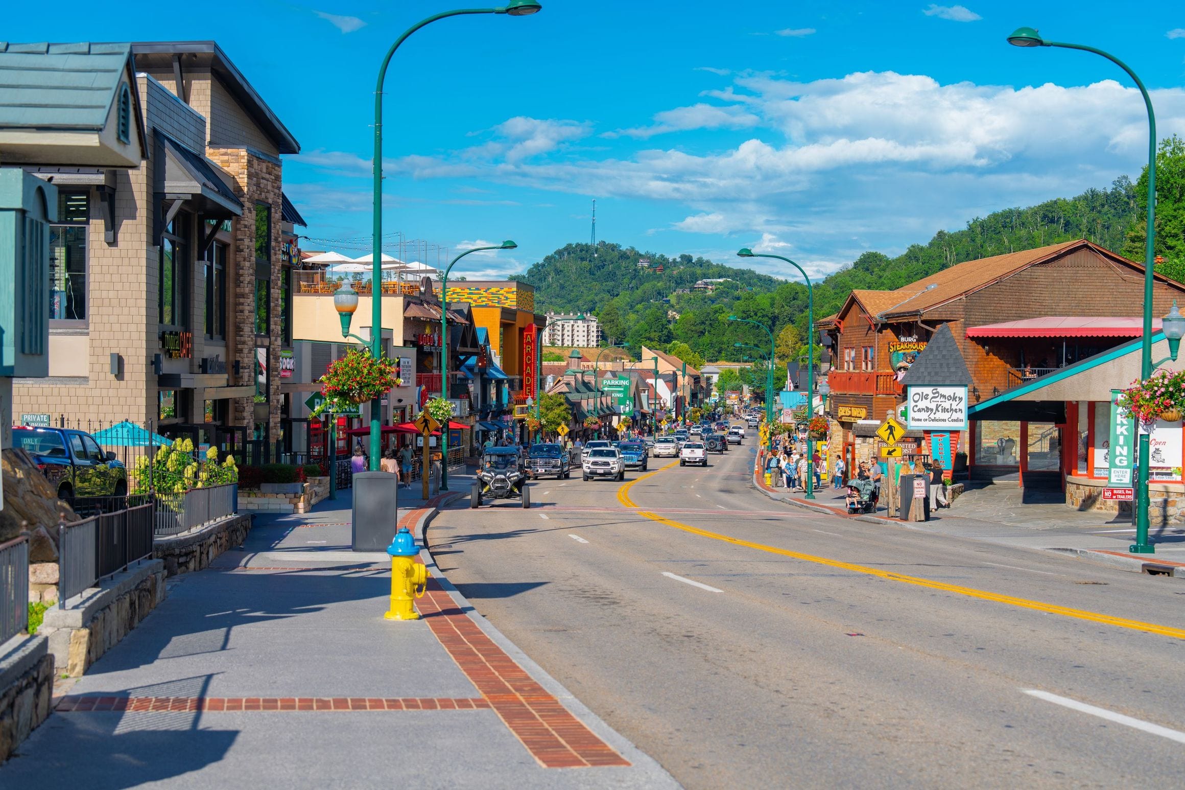 Shops and sidewalk along the main street of Gatlinburg, Tennessee, with Smoky Mountain foothills rising behind the town