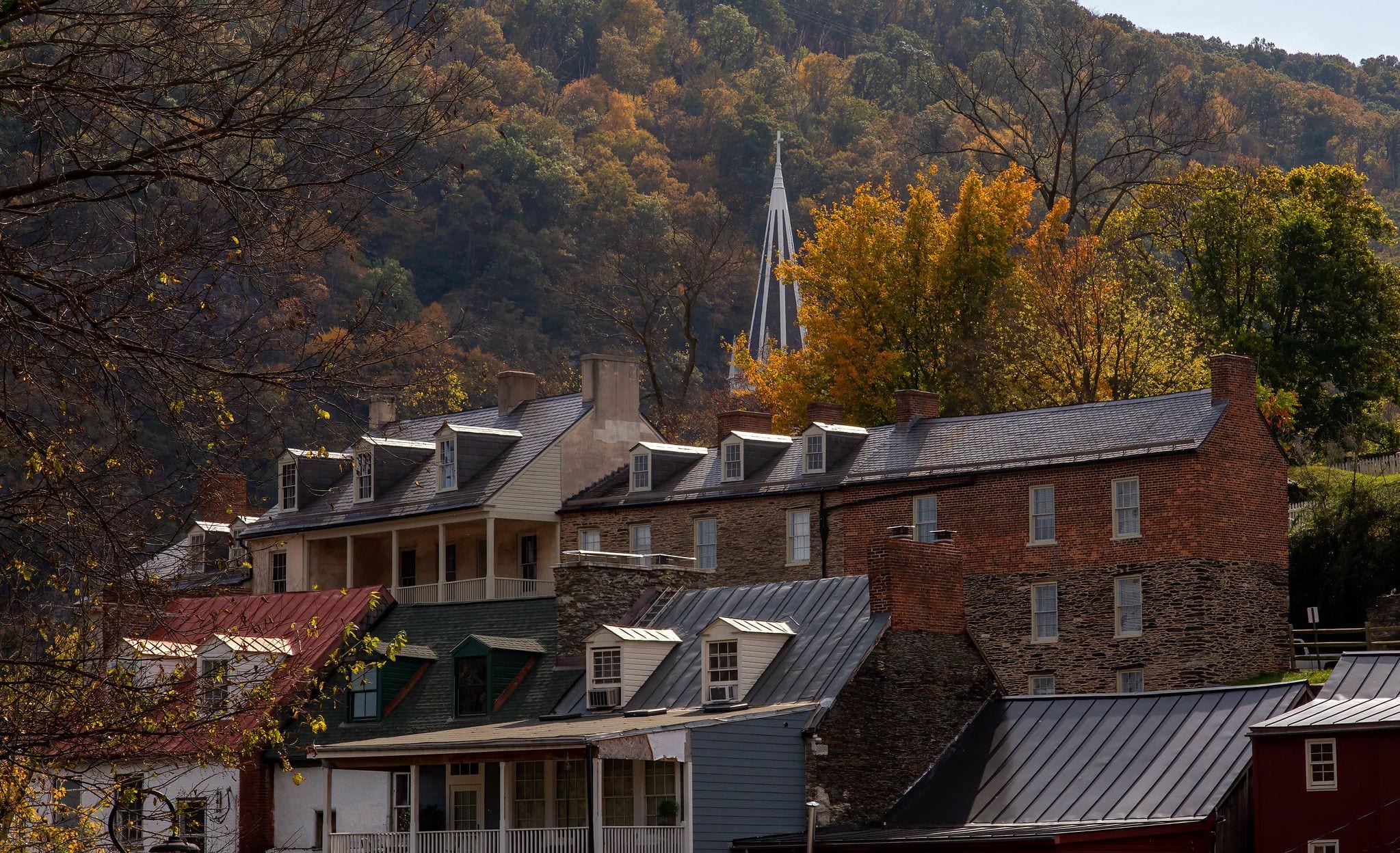 Historic brick and stone buildings of Harpers Ferry's Lower Town in fall color, with a church steeple rising above the wooded hillside, West Virginia