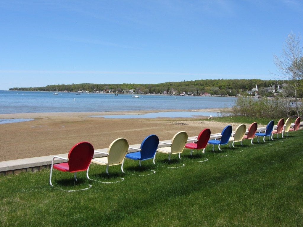Rainbow-colored lawn chairs on the beach at Ephraim, with Eagle Harbor and the wooded Door County shoreline across the water
