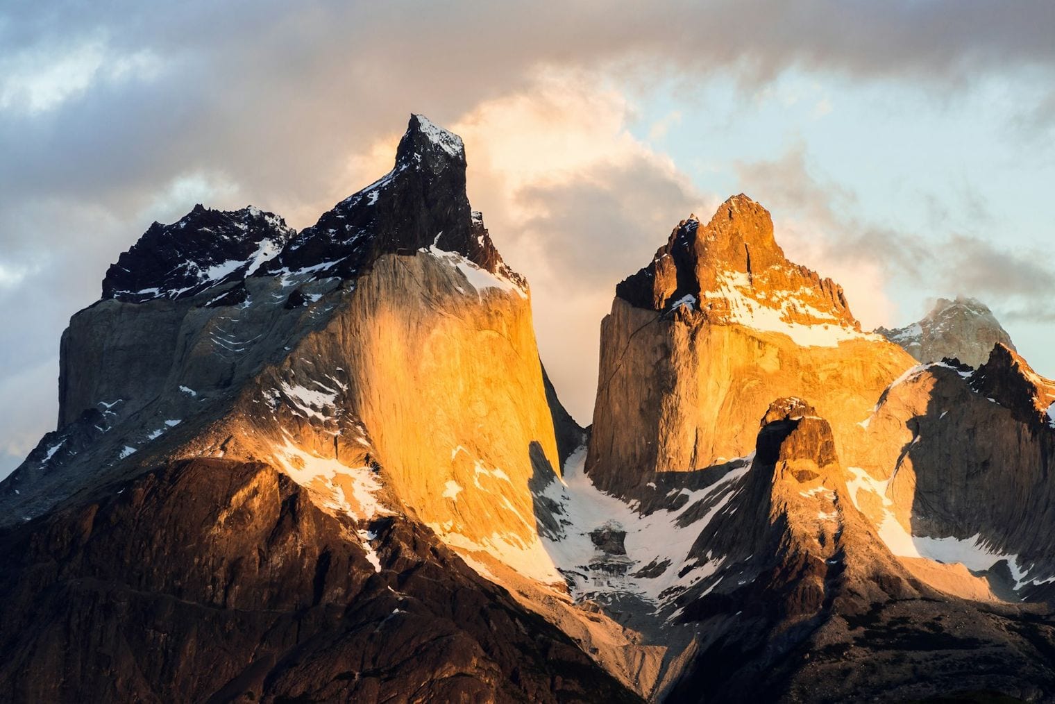 Sheer granite walls glowing orange at sunrise beneath dark rock summits, with snow gathered in the gullies and cloud drifting behind the peaks.