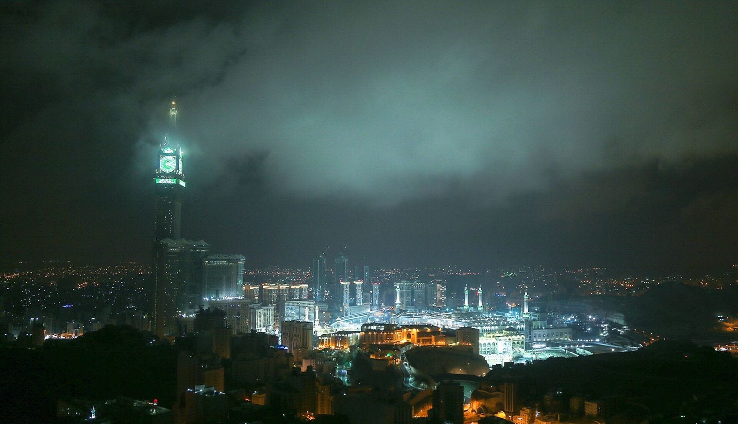 The illuminated Makkah Royal Clock Tower rising above the lights of Mecca at night, its four clock faces glowing green above the Great Mosque.