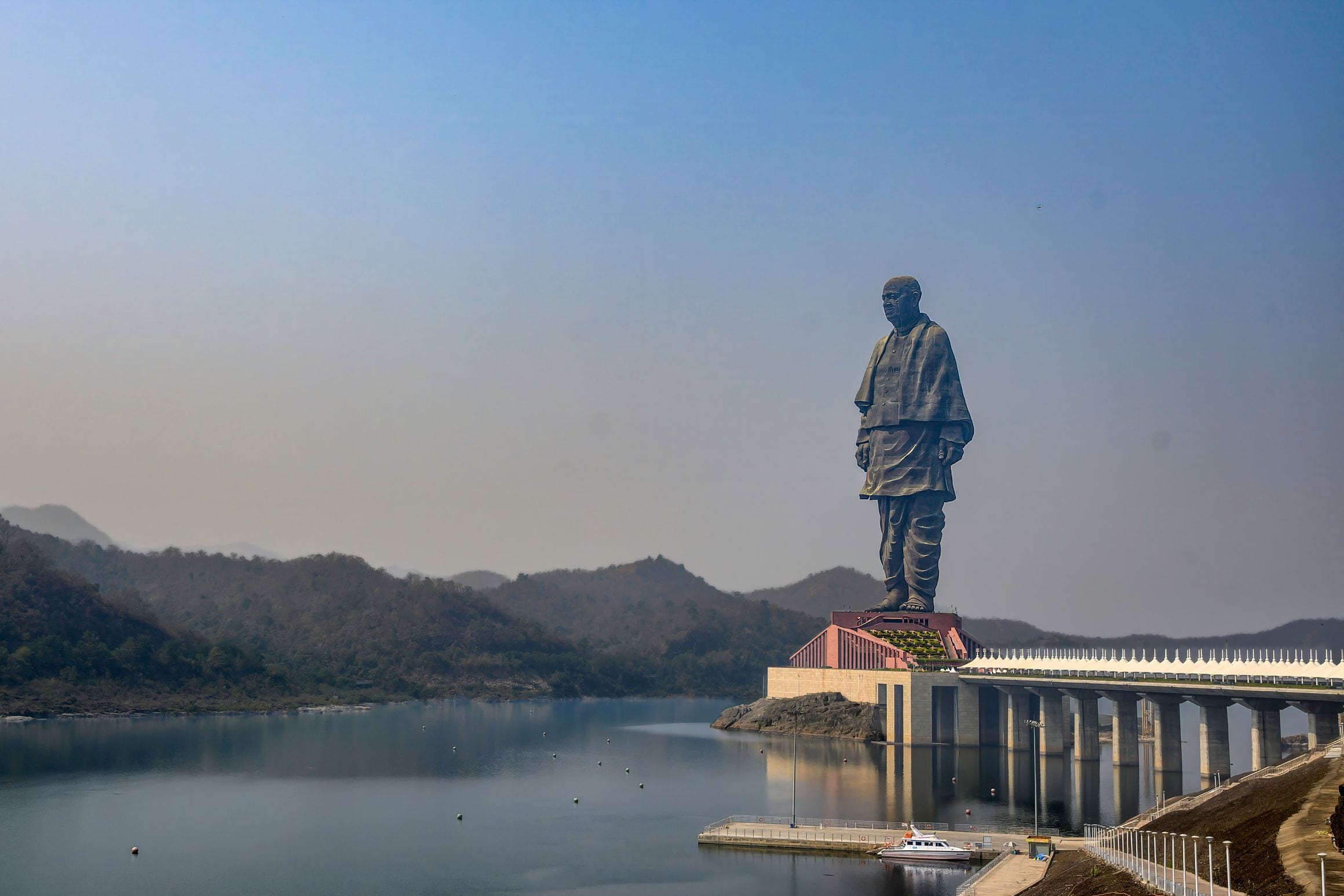 The bronze-clad Statue of Unity towering over its island pedestal and the Narmada River near Kevadia, Gujarat, with wooded hills behind