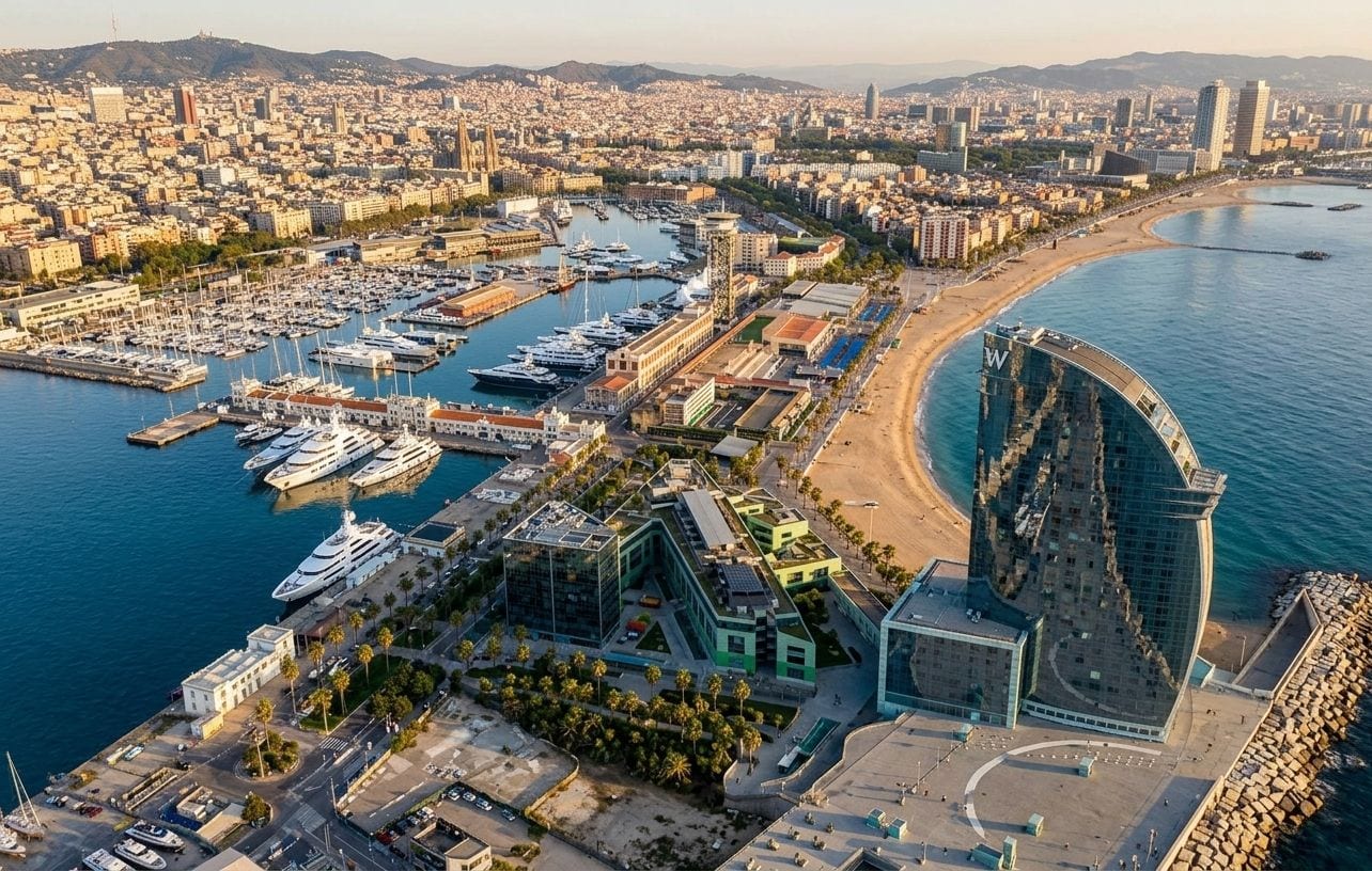Aerial view of the Barcelona waterfront, with the marina and its yachts, Barceloneta beach and the city rising toward the Collserola hills behind
