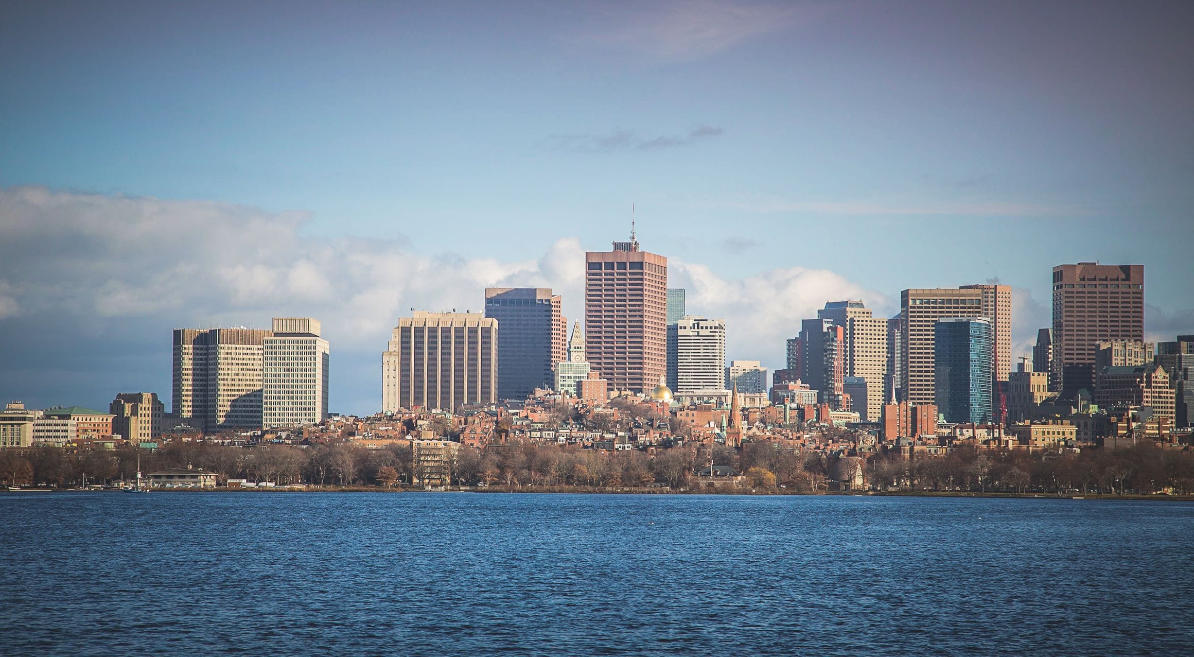 Boston skyline across the Charles River with Back Bay towers under a hazy blue sky