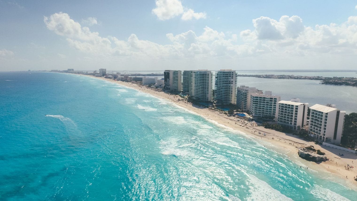 Aerial view of Cancun's Hotel Zone, a narrow white-sand barrier island lined with resort towers between the turquoise Caribbean and the lagoon behind it