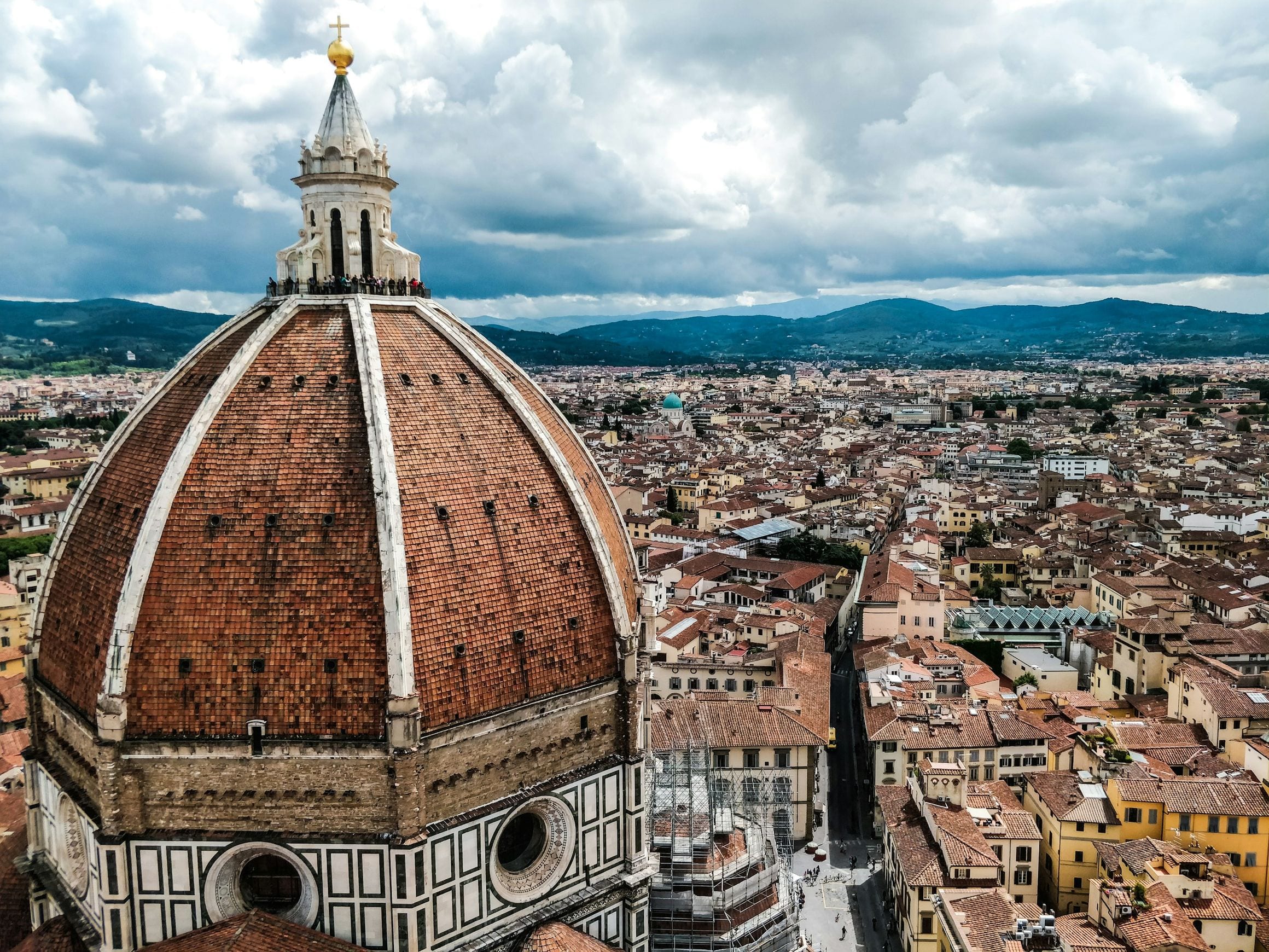 The brick dome of Florence Cathedral rising above the terracotta rooftops of the city, with the Tuscan hills on the horizon