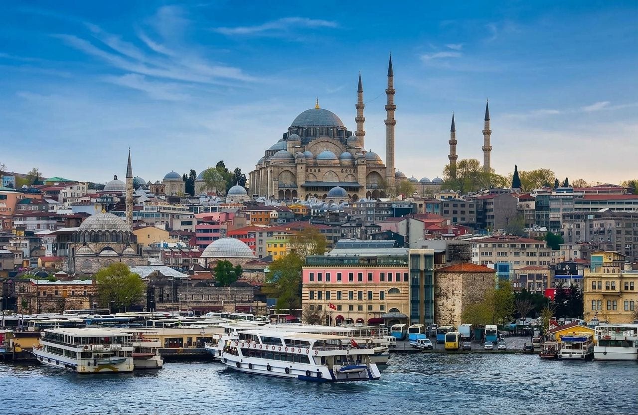 The domes and chimneys of the Suleymaniye Mosque complex above the Golden Horn, with ferries crossing the water and the Galata Tower on the far ridge.