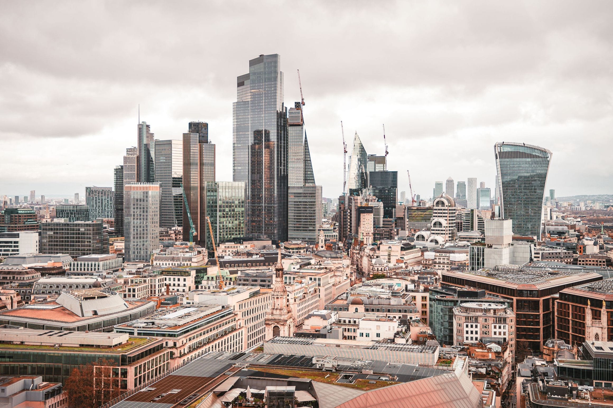 The City of London skyline seen from above, its cluster of glass towers rising over older rooftops beside the Thames
