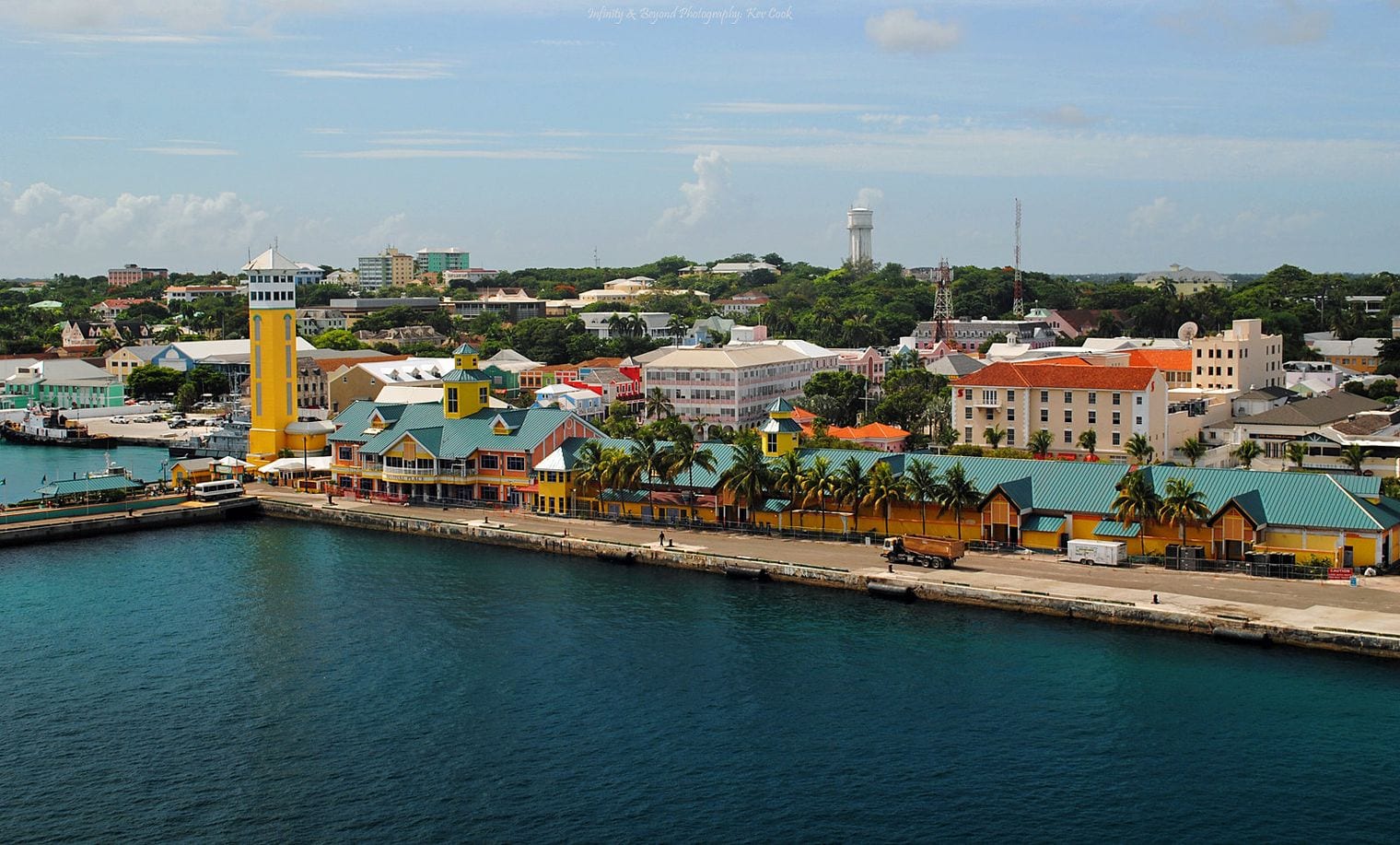 Nassau waterfront seen from the harbour, with the yellow Festival Place tower and green-roofed pavilions along Prince George Wharf backed by pastel colonial buildings