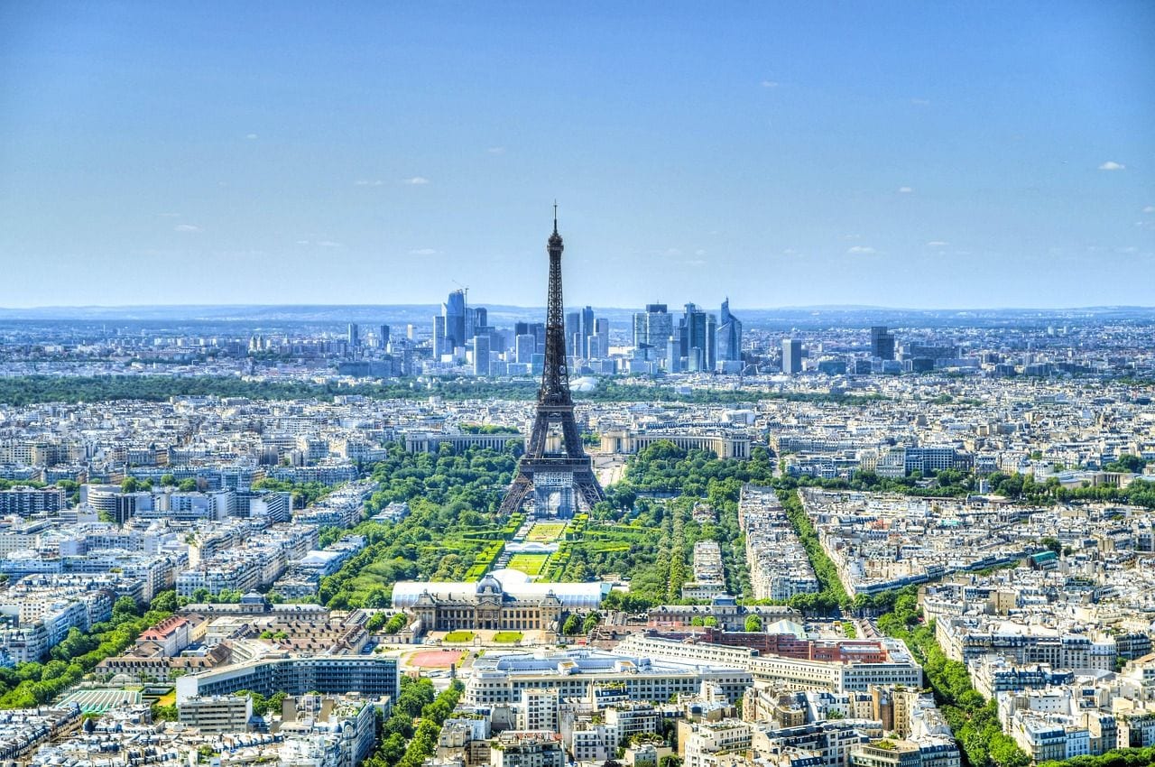 Aerial view over Paris with the Eiffel Tower at the centre, the Champ de Mars below it and the La Defense towers beyond