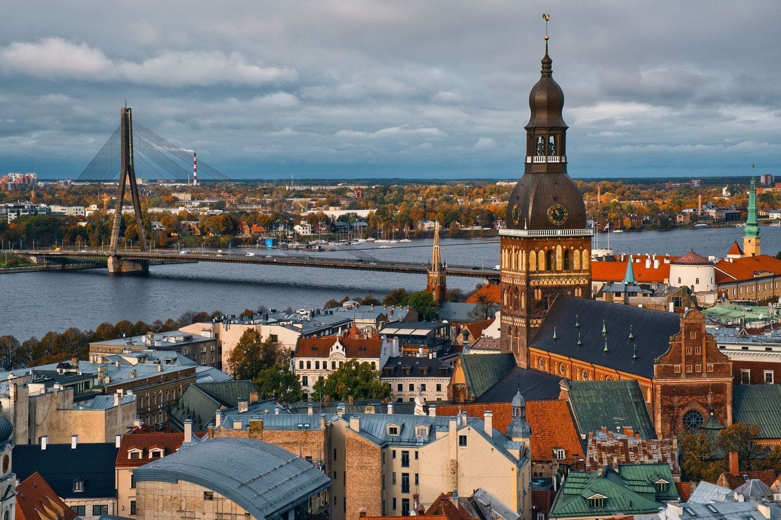 Elevated view over the red rooftops of Riga Old Town, with the tower of Riga Cathedral and the Daugava river beyond