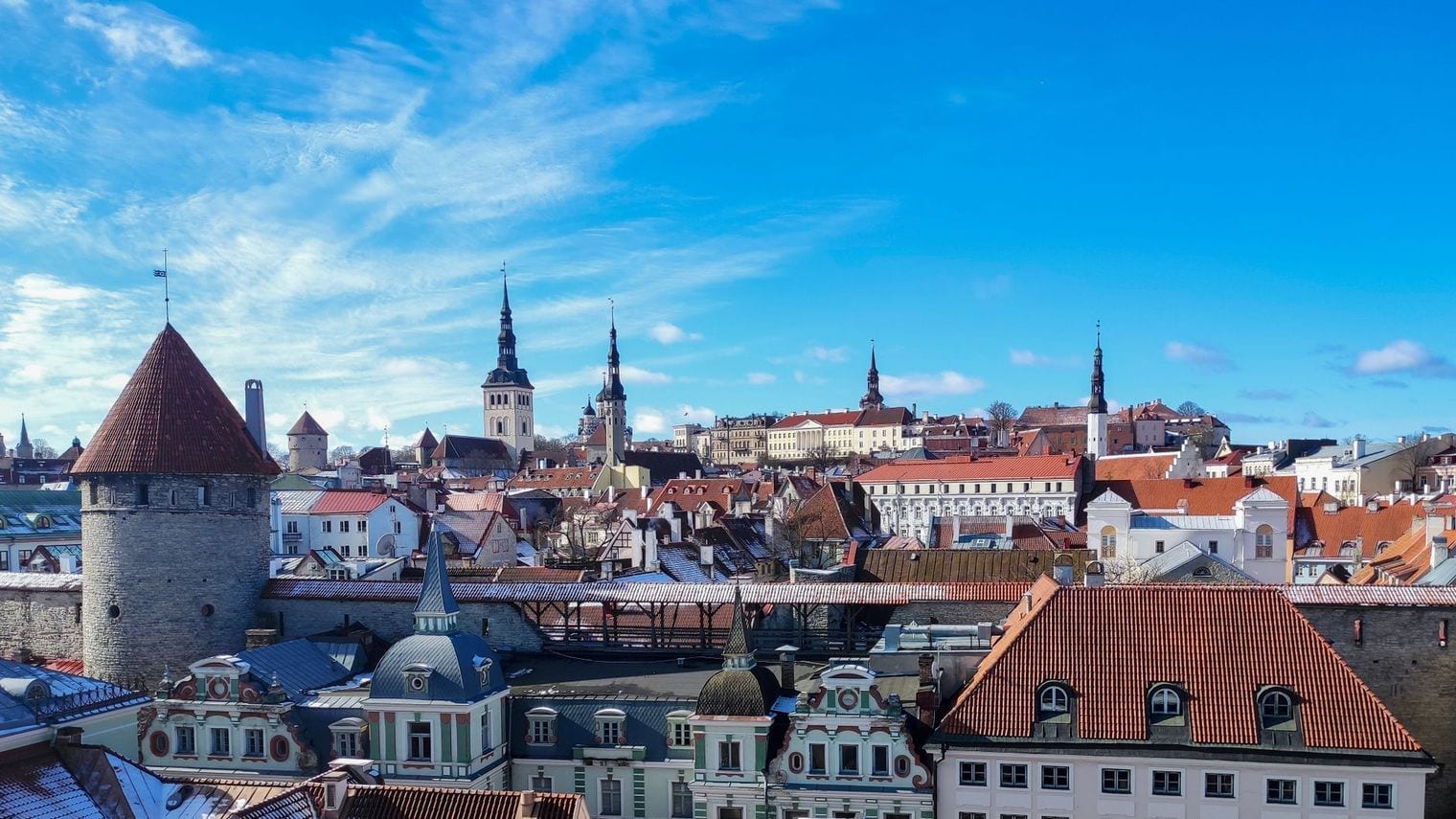 Red-tiled rooftops, medieval wall towers and church spires of Tallinn Old Town under a blue sky