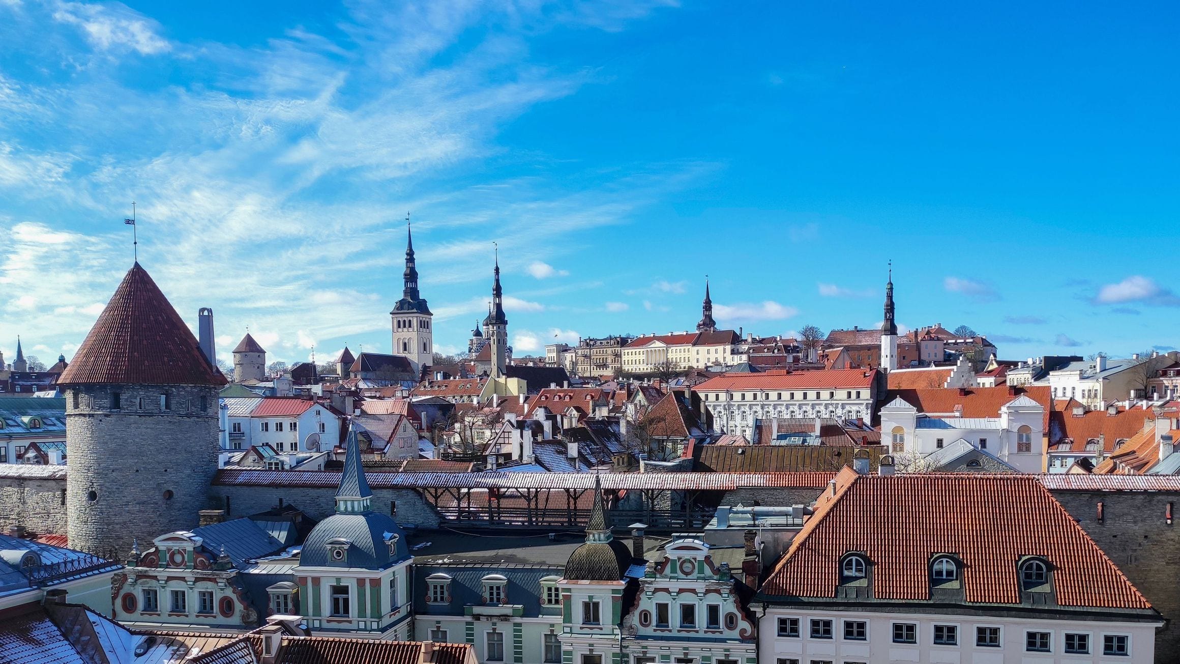 Red-tiled rooftops, medieval wall towers and church spires of Tallinn Old Town under a blue sky