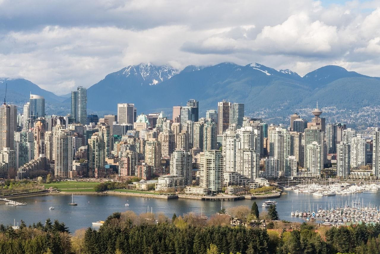Downtown Vancouver towers and a marina on False Creek, with the snow-capped North Shore mountains rising behind the city.