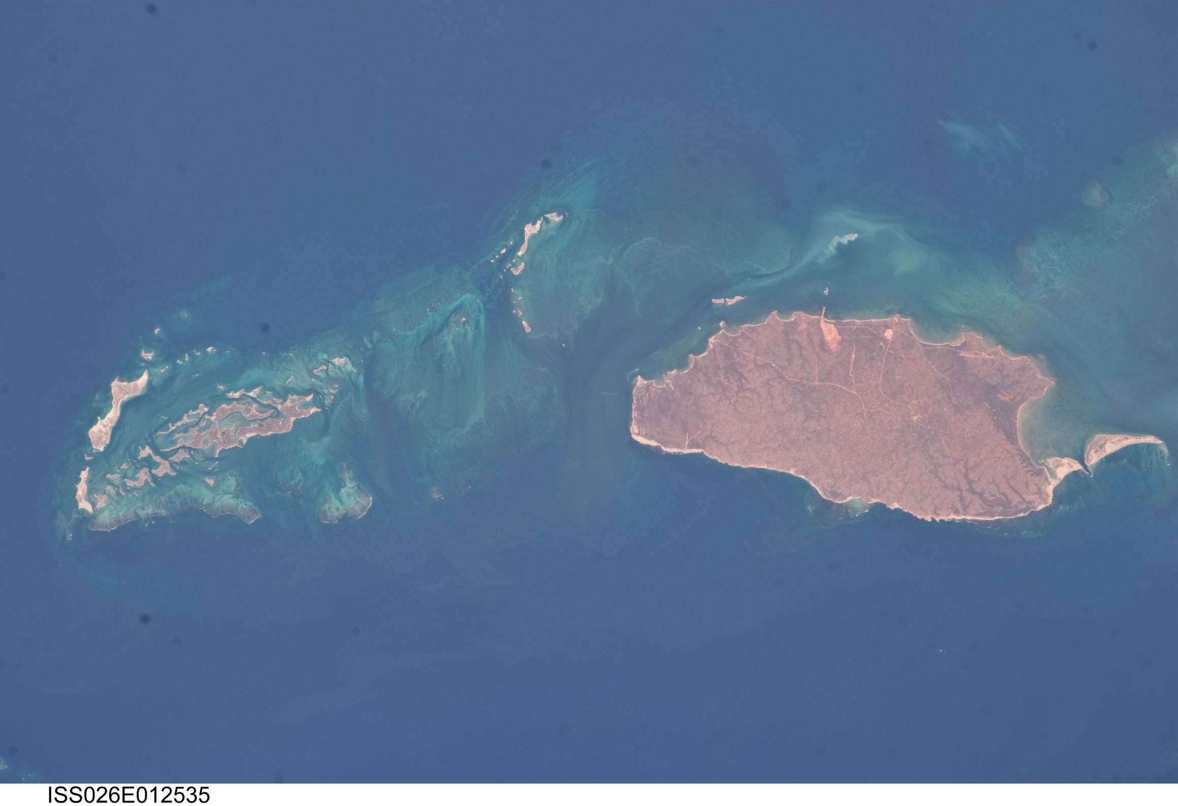 Barrow Island's red, road-scored plateau seen from the International Space Station beside the reef-fringed Montebello Islands off Western Australia